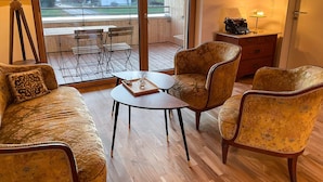 Une pièce comprenant un canapé, deux fauteuils, une petite table, une lampe et donnant sur un balcon équipé d’une table et de chaises.