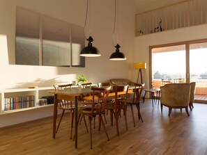 Ein moderner Essbereich mit Holztisch und -stĂŒhlen, Pendelleuchten, einem BĂŒcherregal und Blick durch groĂe Fenster.