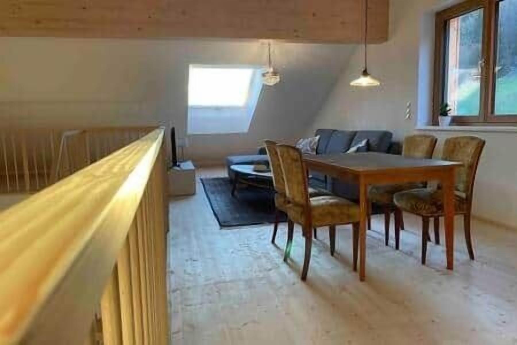 A loft-style room with a dining table and chairs, a sofa, and a large window.