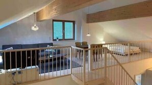 Une pièce de style loft avec un plafond haut, une poutre en bois, un lit, un canapé et une fenêtre.