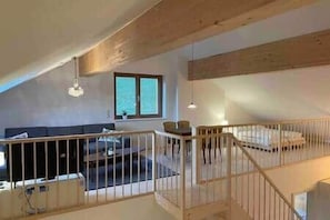 Ein Loft-Zimmer mit hohen Decken, einem Holzbalken, einem Bett, einer Couch und einem Fenster.