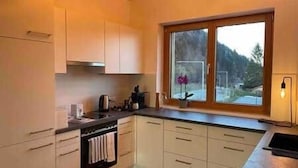 A kitchen with white cabinets, a stove, and a window with a view of the outdoors. - Gamsfels Josephine gallery apartment (Langen bei Bregenz)