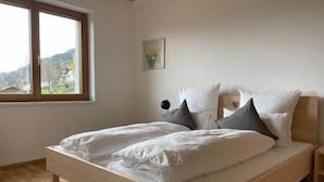 Une chambre à coucher avec un lit en bois, du linge de lit blanc, une fenêtre donnant sur un beau paysage et une petite table de chevet.