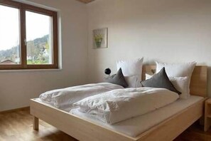 Ein Schlafzimmer mit einem hölzernen Bett, weiĂer BettwĂ€sche, einem Fenster mit Ausblick und einem kleinen Nachttisch.