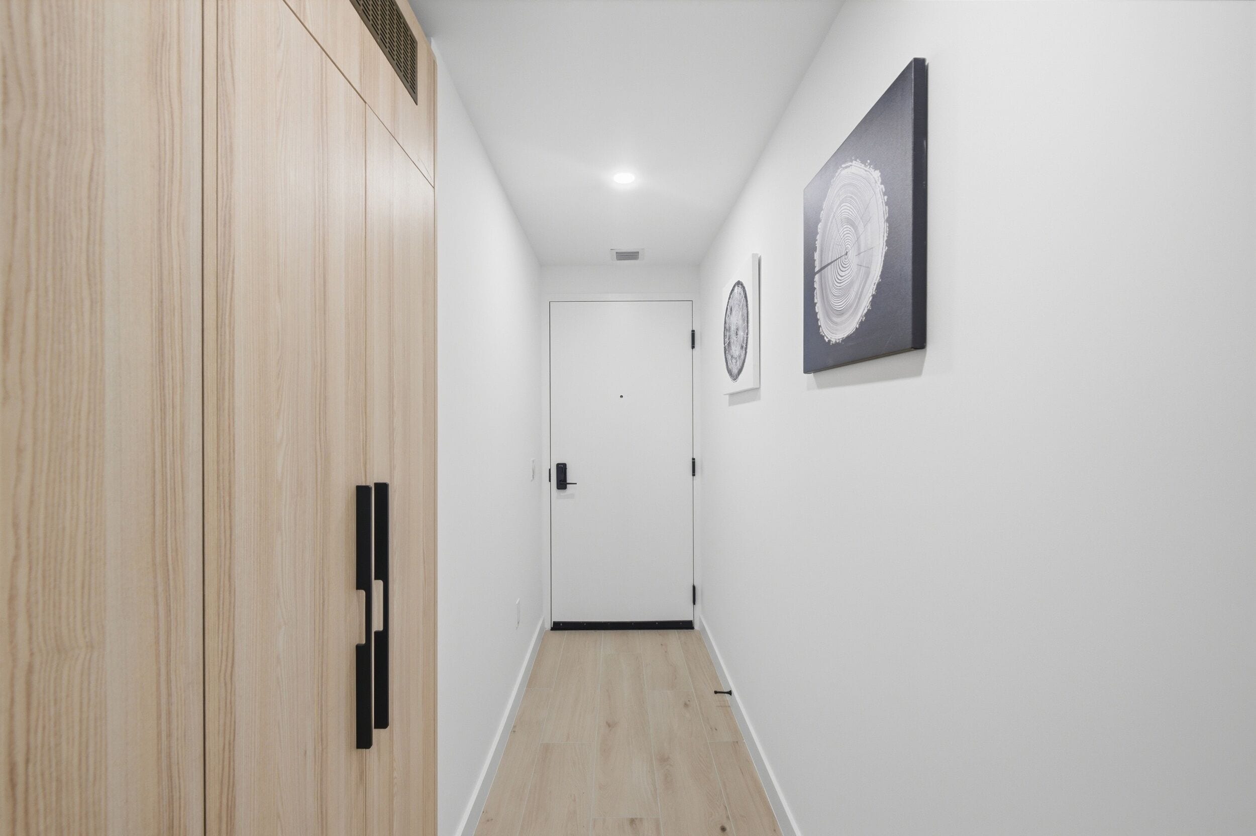 Un pasillo con un armario de madera, una puerta blanca y dos cuadros en la pared.