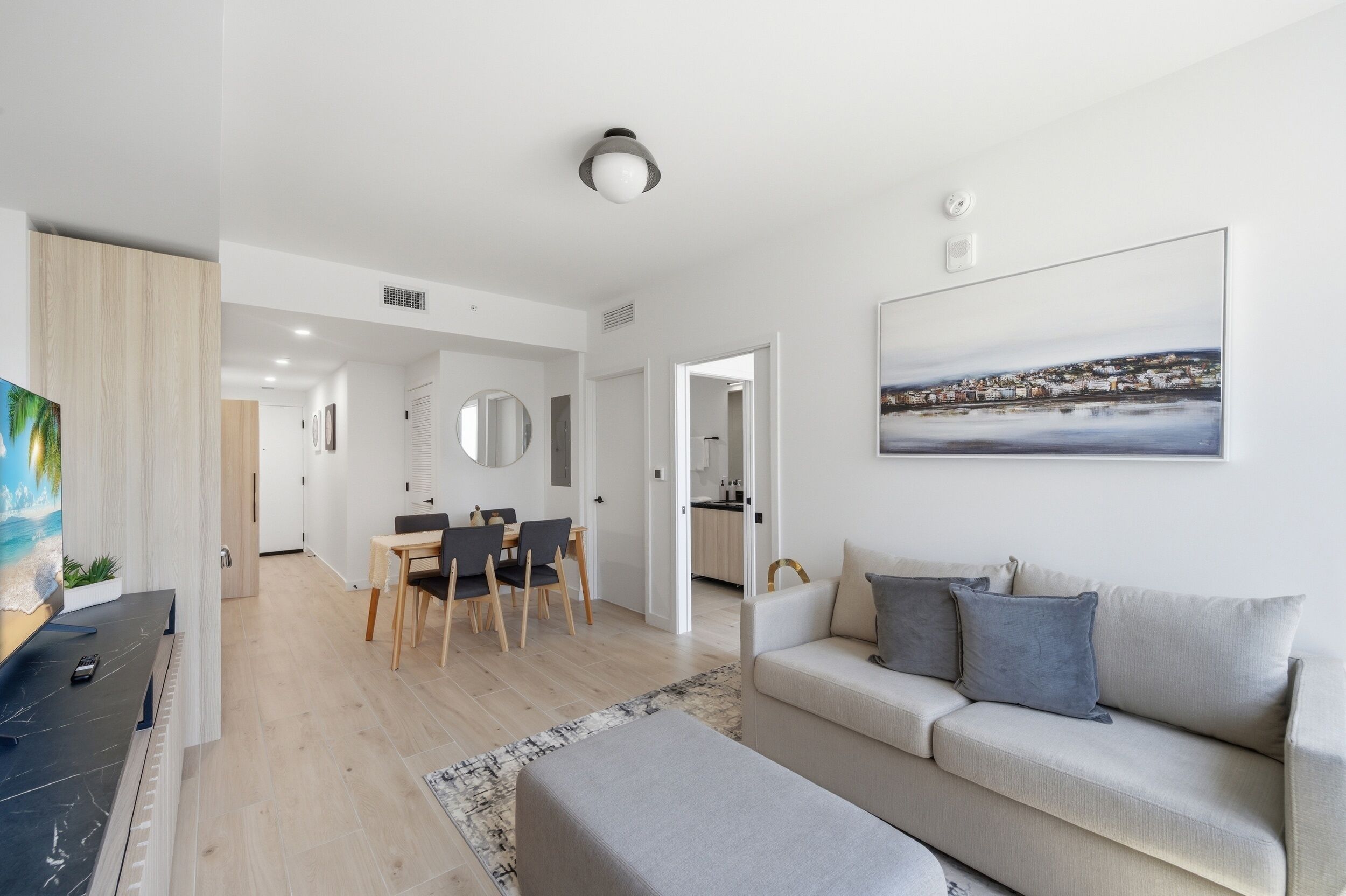 A modern living room with a sofa, a dining area with chairs, a TV, and a painting on the wall.