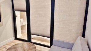 Una stanza con una porta scorrevole che dà su un bagno, un divano chiaro e un tavolo rotondo in legno.