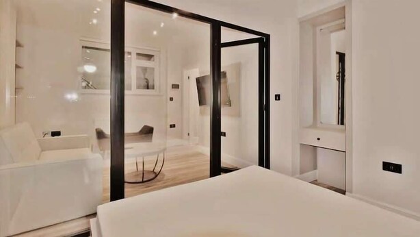 Una camera d'albergo moderna con un letto, un divano, una parete divisoria in vetro e una televisione.