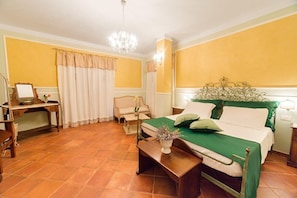 A hotel room with a bed, a desk, a chair, a small table with a vase, and a chandelier.