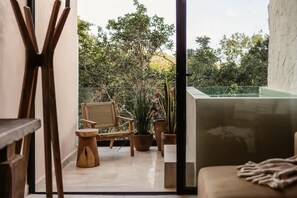 Ein Balkon mit einem Korbstuhl, einem kleinen Holzschemel und Topfpflanzen.