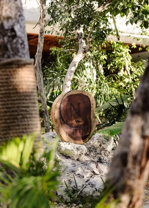 A wooden sign with the letter 'N' and the word 'NUUP' carved into it, placed on a rock in a garden setting. - Nuup Pomona Romantic Jungle Loft Beach Club Access (Tulum)