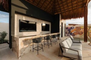 An outdoor bar area with a stone countertop, two TVs, bar stools, and a sofa. - Nuup Pomona Romantic Jungle Loft Beach Club Access (Tulum)