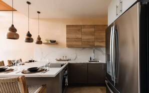 Eine moderne Küche mit Marmorarbeitsplatte, dunklen Schränken und einem Edelstahl-Kühlschrank.