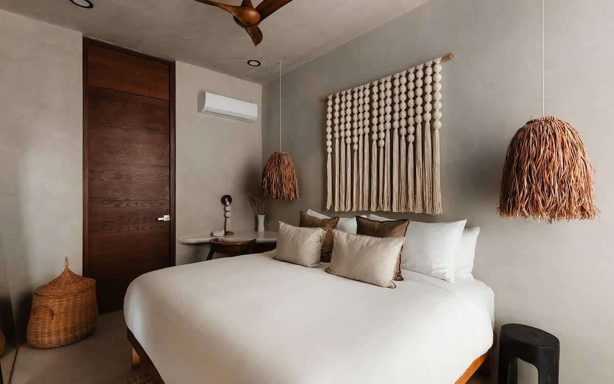 Une chambre à coucher avec un lit, une porte en bois, une décoration murale en macramé et un luminaire en fibres tressées.