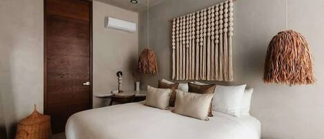 Une chambre à coucher avec un lit, une porte en bois, une décoration murale en macramé et un luminaire en fibres tressées.