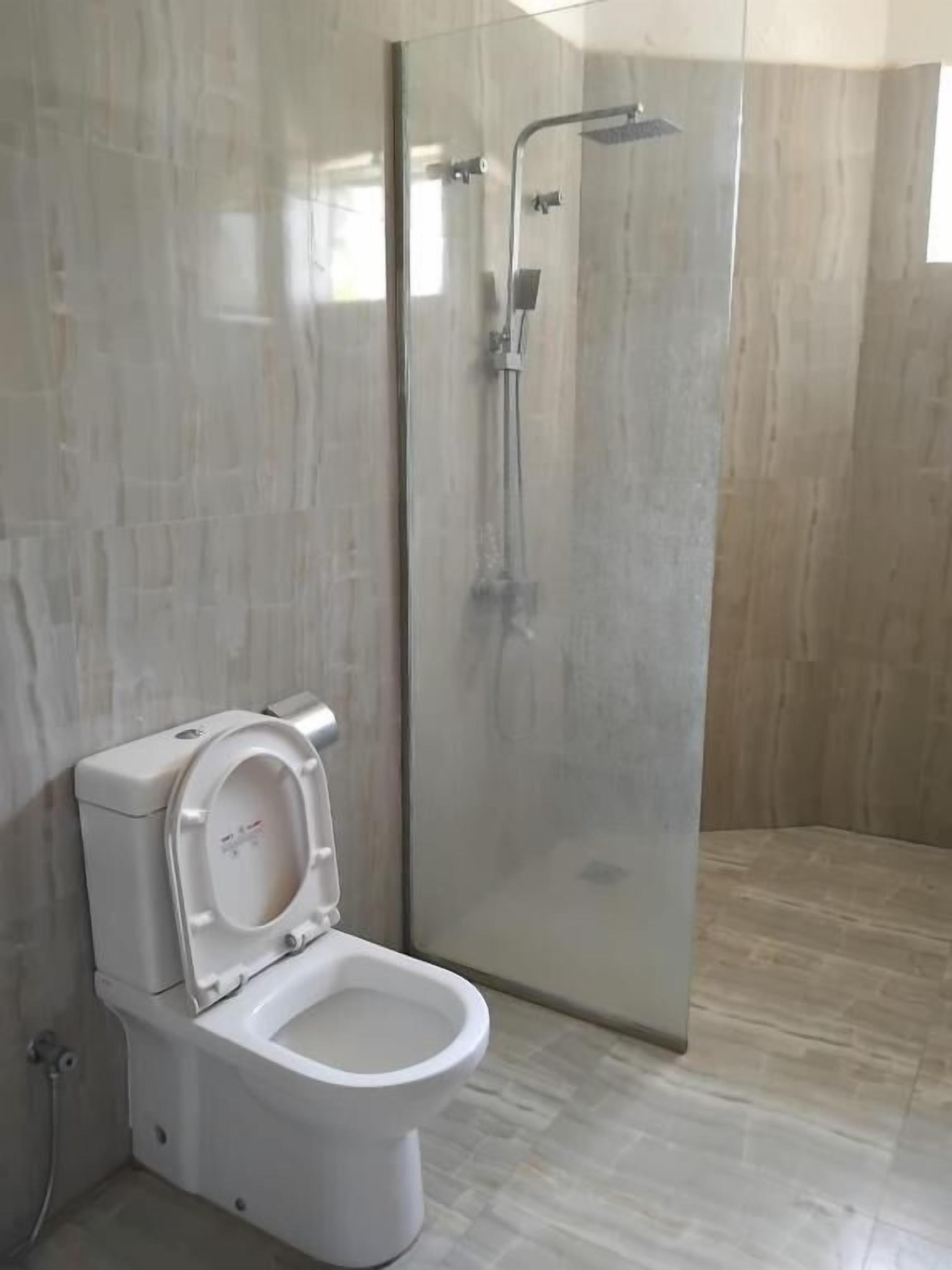A bathroom with a toilet, a glass shower enclosure, and a tiled floor.