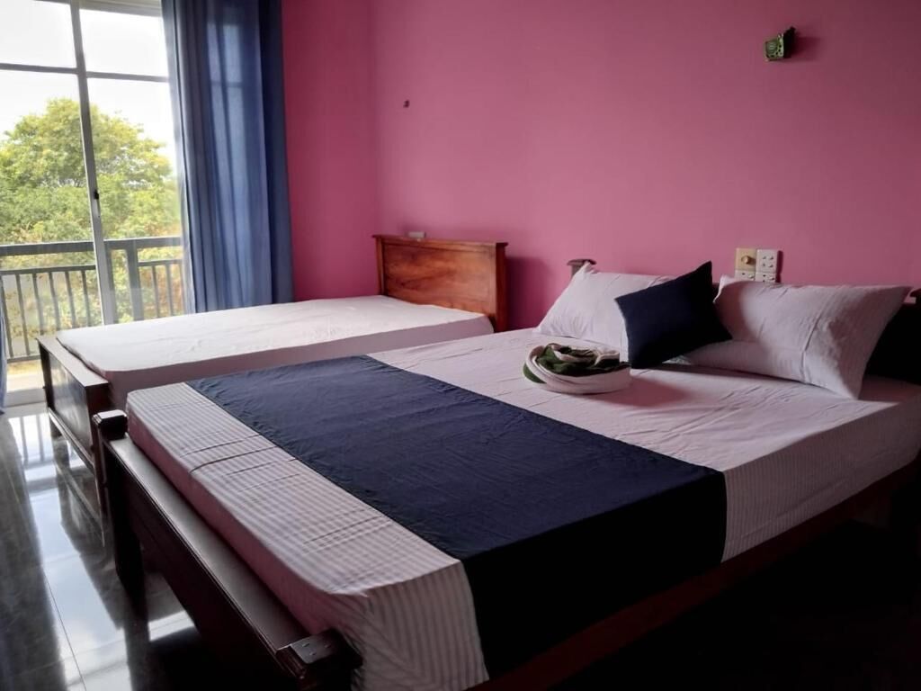 A room with two beds, a wooden headboard, a nightstand, and a window with a view of trees.