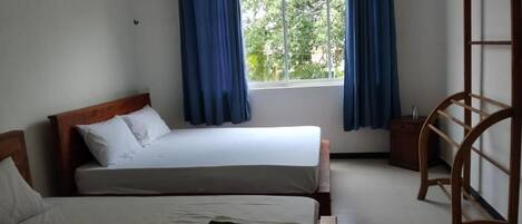 A bedroom with two beds, a window with curtains, and a wooden shelf.