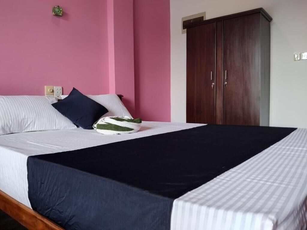 Un lit avec une couverture sombre, des oreillers et une serviette verte et blanche. Une armoire en bois est adossée au mur.