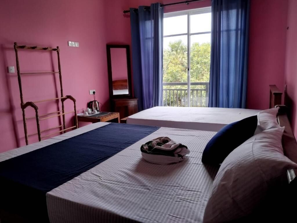 A bedroom with two beds, a window with curtains, a wooden ladder, and a small table with a lamp.