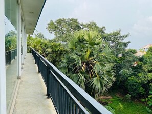 A balcony with a railing, a concrete floor, and dense greenery including palm trees. - Esha Beach Resort - Trincomalee (Trincomalee)