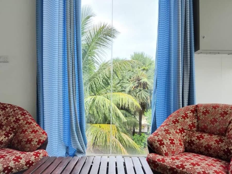 A room with a view of palm trees, two patterned chairs, and a wooden table.