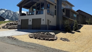 Ett modernt hus i två våningar med en inglasad veranda, garageportar och en välanlagd trädgård framför huset, inklusive en eldstad.