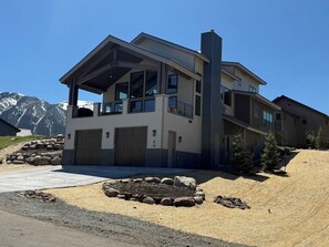 Ein modernes, zweistöckiges Haus mit überdachter Veranda, Garagentoren und einem begrünten Vorgarten mit Feuerstelle.