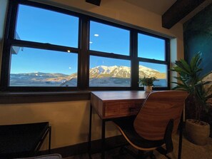 Ein Zimmer mit Schreibtisch und Stuhl, vor einem großen Fenster mit Blick auf die Berge.
