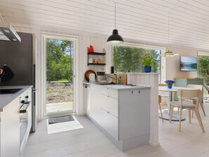 Eine moderne Küche mit einer zentralen Kochinsel, einem Essbereich mit Stühlen und einem an der Wand montierten Fernseher.