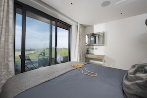 Ein Schlafzimmer mit großem Fenster, einem Bett, einem Nachttisch, einem Spiegel und Blick auf einen Golfplatz.