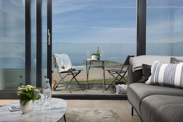 Ein Balkon mit Blick auf den Strand, ein Tisch mit Flasche und Gläsern sowie eine Couch mit Decke.