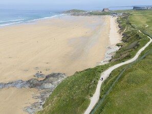 Ein Küstenstrand mit einem Gehweg entlang der Uferlinie, einer Grünfläche und einem Gebäude im Hintergrund.