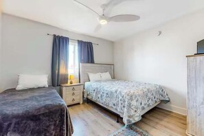 A bedroom with two beds, a nightstand, a lamp, a ceiling fan, and a wardrobe.