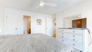 Ein Schlafzimmer mit Bett, Schminktisch, Deckenventilator und einer Tür zu einem anderen Raum.