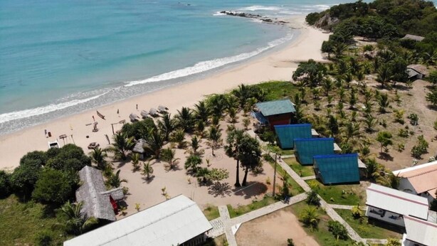 Vista aérea de un complejo turístico en la playa, con una playa arenosa, palmeras y varios edificios con techos azules.
