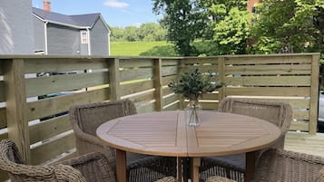 A round wooden table with wicker chairs, a wooden fence, and a view of a green landscape.