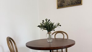 Una mesa redonda de madera con dos sillas, un jarrón con plantas y un cuadro en la pared.