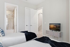 Une chambre avec deux lits, un téléviseur posé sur un meuble blanc, et une douche visible à travers une porte ouverte.