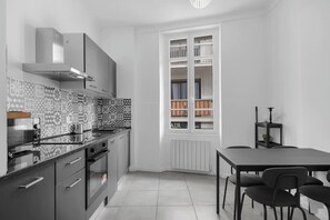 Eine moderne Küche mit Einbauofen, Herd und Mikrowelle. Ein Esstisch mit Stühlen und ein Fenster mit Blick ins Freie.