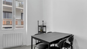 Una habitación moderna y minimalista con una mesa gris y cuatro sillas, un radiador y una ventana con vistas a un balcón.