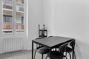 Ein moderner, minimalistischer Raum mit einem grauen Tisch, vier Stühlen, einer Heizung und einem Fenster mit Blick auf einen Balkon.