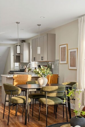 A modern kitchen with a dining area, featuring a central island, pendant lights, and a view of the living room. - Spacious 7BD/7BR Home in Somerville, 10 mins to Boston, Harvard, MIT (Somerville)