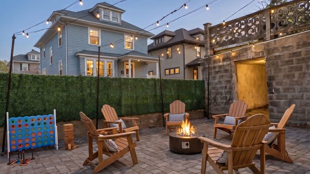 A patio with wooden chairs and a fire pit, surrounded by a hedge and a brick wall. - Spacious 7BD/7BR Home in Somerville, 10 mins to Boston, Harvard, MIT (Somerville)