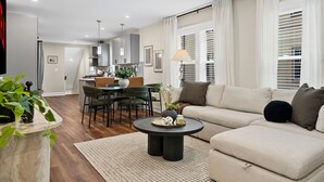 A modern living room with a sofa, a round coffee table, and a dining area with chairs and a table. - Spacious 7BD/7BR Home in Somerville, 10 mins to Boston, Harvard, MIT (Somerville)