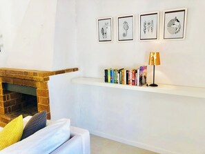 A living room with a brick fireplace, a white sofa with cushions, a bookshelf with books, and framed artwork on the wall.