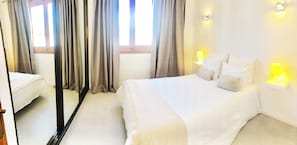 A hotel room with a bed, bedside lamps, a window with curtains, and a door.