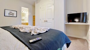 Een slaapkamer met een bed, een televisie, een plafondventilator en een deur.