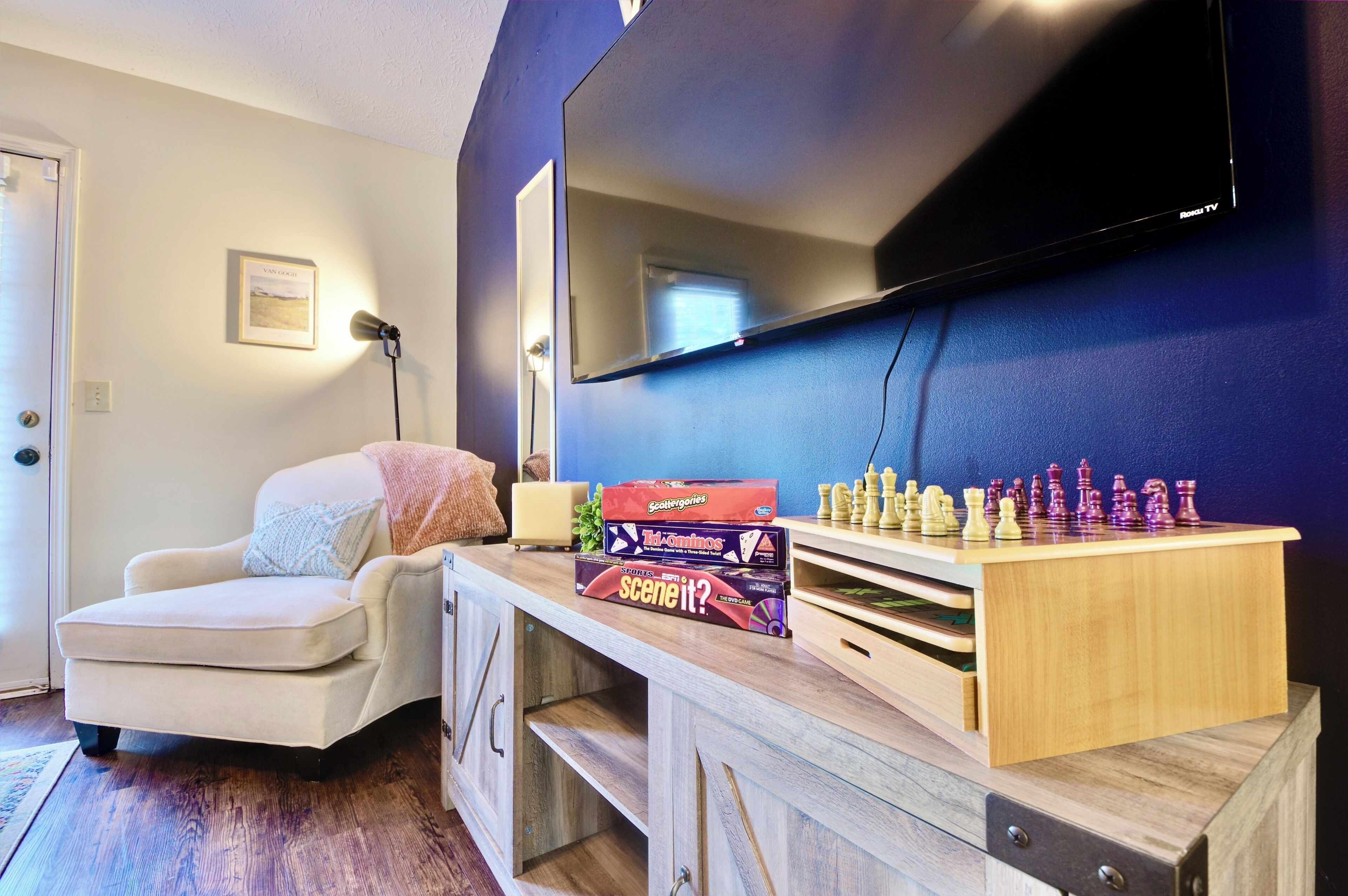 Een kamer met een aan de muur bevestigde televisie, een houten bureau met schaakstukken en een stoel.