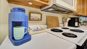 Een keuken met een koffiezetapparaat, een mok, een dienblad met koffiecups, een fornuis en houten kastjes.